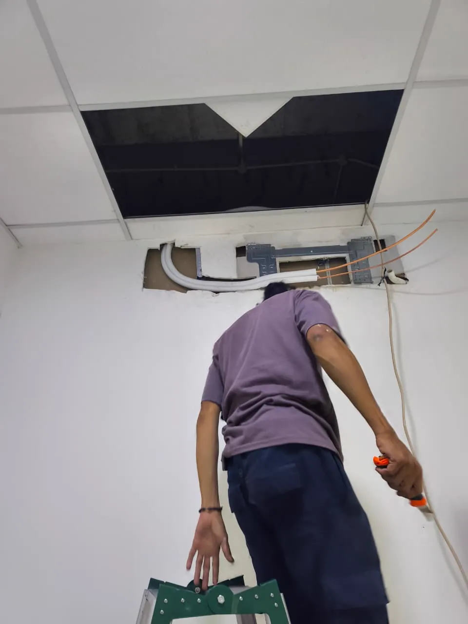 Teknisi memasang jalur pipa tembaga dan braket logam di dinding untuk unit indoor AC