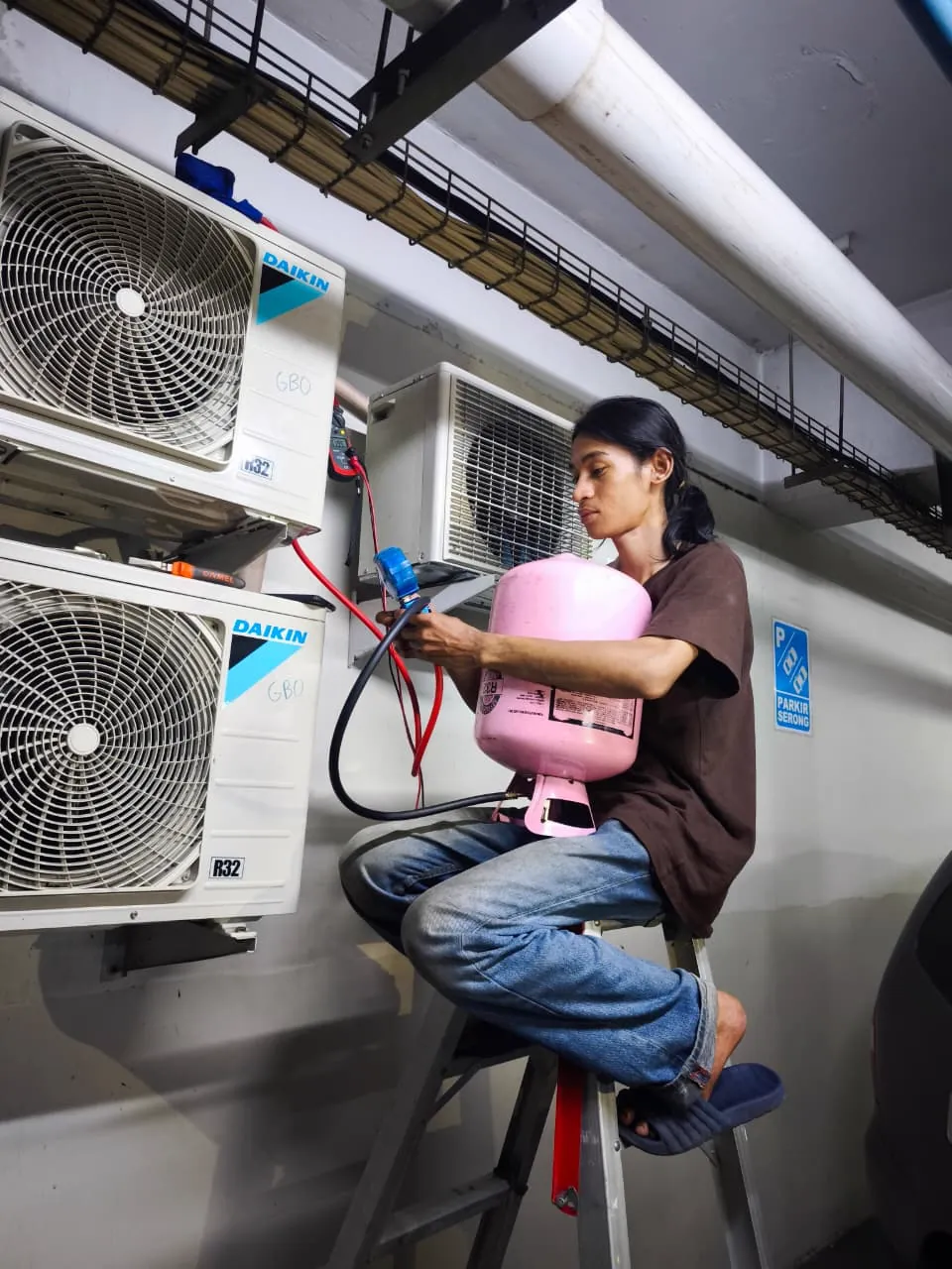 Teknisi mengisi freon AC Daikin dengan manifold gauge di area parkir basement